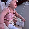 baby, infant, child, portrait, sitting, pink_outfit, knitted_clothing, headband, bow, white_socks, baby_seat, blanket, indoor, cozy, looking_up, profile, face, arms, legs, soft_lighting