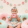 baby, child, donut, plush, pink, sprinkles, headband, dress, sitting, smiling, cute, indoor, decor, pastel_colors, toy, foot, happy, playful, portrait, celebration