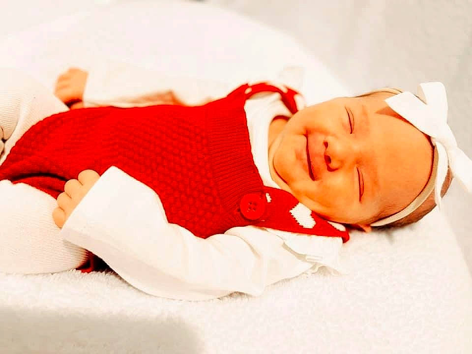 Rosalie is registered to the contest to win money with this photo: baby, baby_products, baby_sleeping, baby_toddler_clothing, carmine, child, comfort, elbow, happy, hat, headwear, human_body, human_leg, laugh, linens, person, portrait_photography, room, sleeve, smile