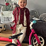 child, boy, smiling, balance_bike, indoor, traditional_clothing, wooden_floor, toy, happy, furniture, cushion, high_chair, face, person, floor, room, playful, decor, young, standing