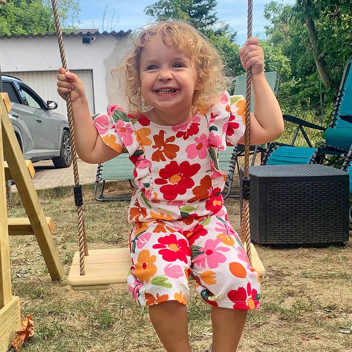 Laura participe au concours pour gagner de l'argent avec cette photo : car, child, clothing, curly_hair, daylight, flower_pattern, garden, grass, happy, joyful, nature, outdoor, person, playground, seat, shoes, smiling, summer, swing, tree