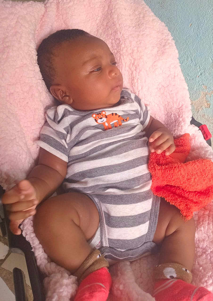 Asaël participe au concours pour gagner de l'argent avec cette photo : baby, infant, onesie, stripes, tiger_patch, pink_blanket, orange_towel, socks, chubby_legs, face, hand, car_seat, bedding, fabric, indoor, wall_texture, portrait, relaxed, looking_away, cute