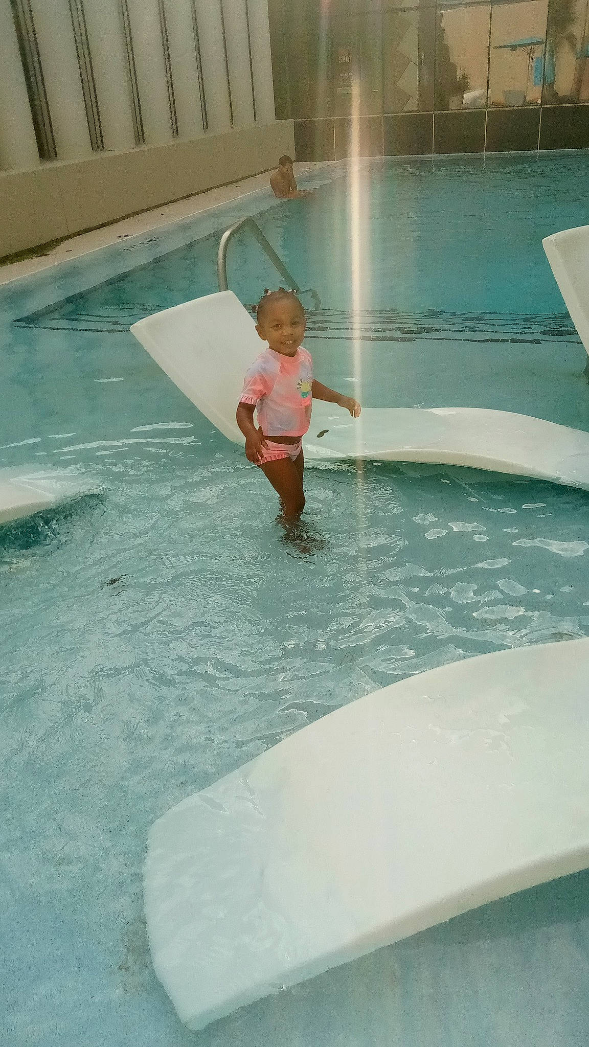 Mallori is registered to the contest to win money with this photo: automotive_exterior, baby, barefoot, cleanliness, composite_material, concrete, floor, flooring, fun, games, glass, joy, leisure, leisure_centre, person, play, recreation, shorts, swimming_pool, toddler