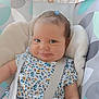 baby, baby_seat, blue_eyes, cheeks, child, closeup, comfort, cushion, cute, floral_clothing, hair_clip, happy, indoors, infant, person, portrait, smile, soft_lighting, straps, young_child