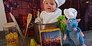 Augustine participe au concours pour gagner de l'argent avec cette photo : apple, baby, blue_rat, chef_hat, child, cooking_pot, costume, cute, floor, fruit, grapes, indoor, kitchen_backdrop, orange, pasta, pear, playful, plush_toy, portrait, wooden_spoons