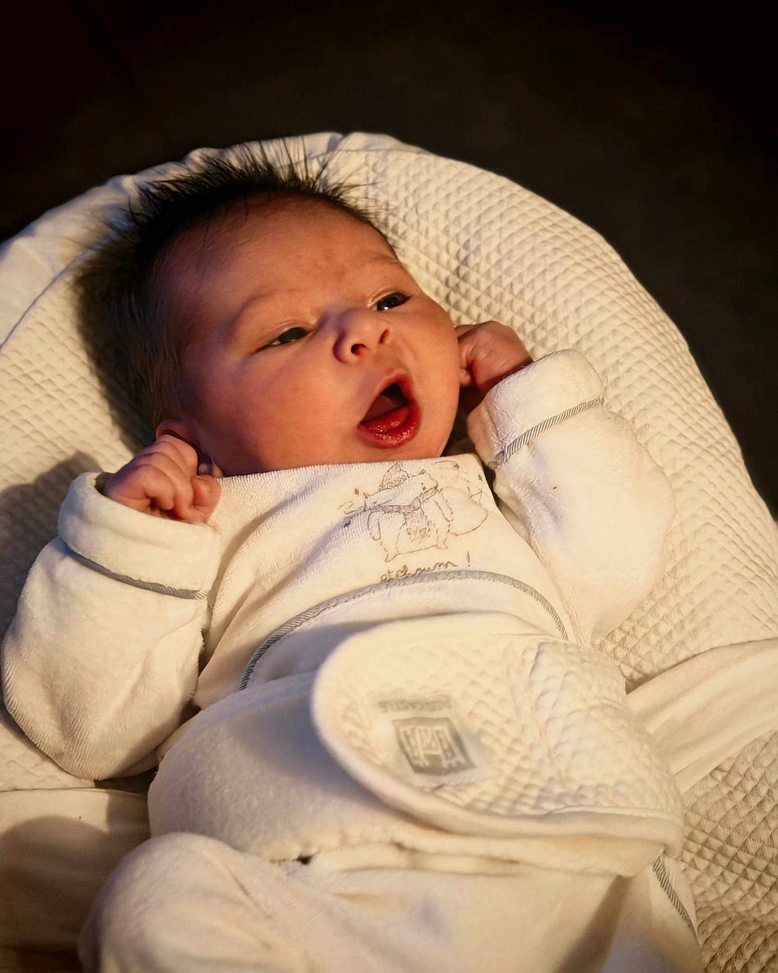 Jules a rejoint le concours — aidez-le/la à gagner de superbes lots ! baby, infant, newborn, white_clothing, soft_fabric, cushion, texture, raised_fists, open_mouth, face, head, sleepwear, indoors, portrait, cute, human, child, lying_down, warm_light, cozy