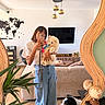 woman, person, dog, puppy, fluffy_dog, black_and_white_dog, tennis_ball, mirror_selfie, smartphone, living_room, interior, sofa, television, plant, world_map, pendant_lights, wooden_floor, globes, fashion, pet