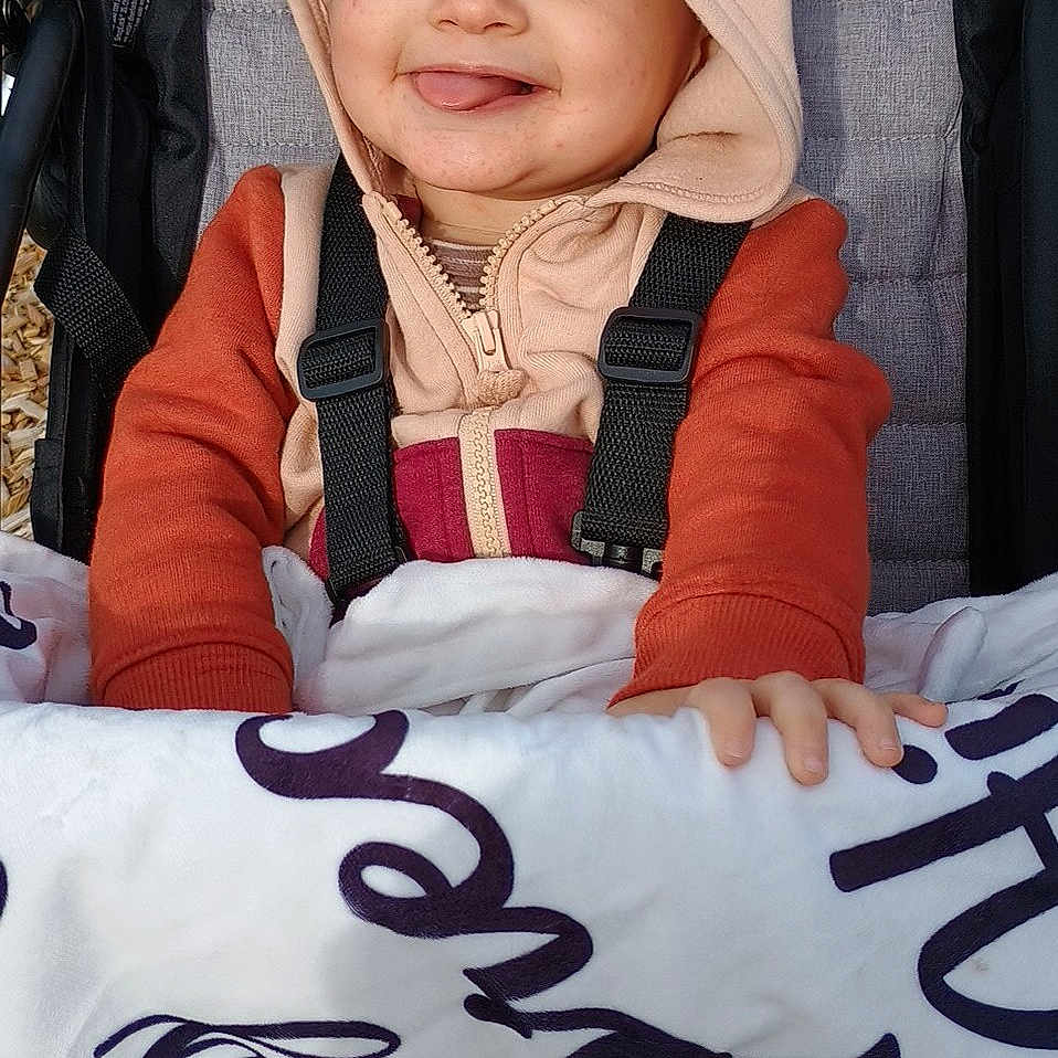 Izaiah is registered to the contest to win money with this photo: baby, bonnet, cap, clothing, coat, cushion, face, happy, hat, head, homedecor, hood, jacket, pants, person, photography, portrait, smile, stroller, text