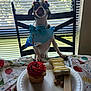 balloon, birthday, blinds, bone, bow_tie, celebration, chair, cupcake, dog, festive, happy, indoor, licking, party_hat, pet, small_dog, table, tablecloth, treats, window