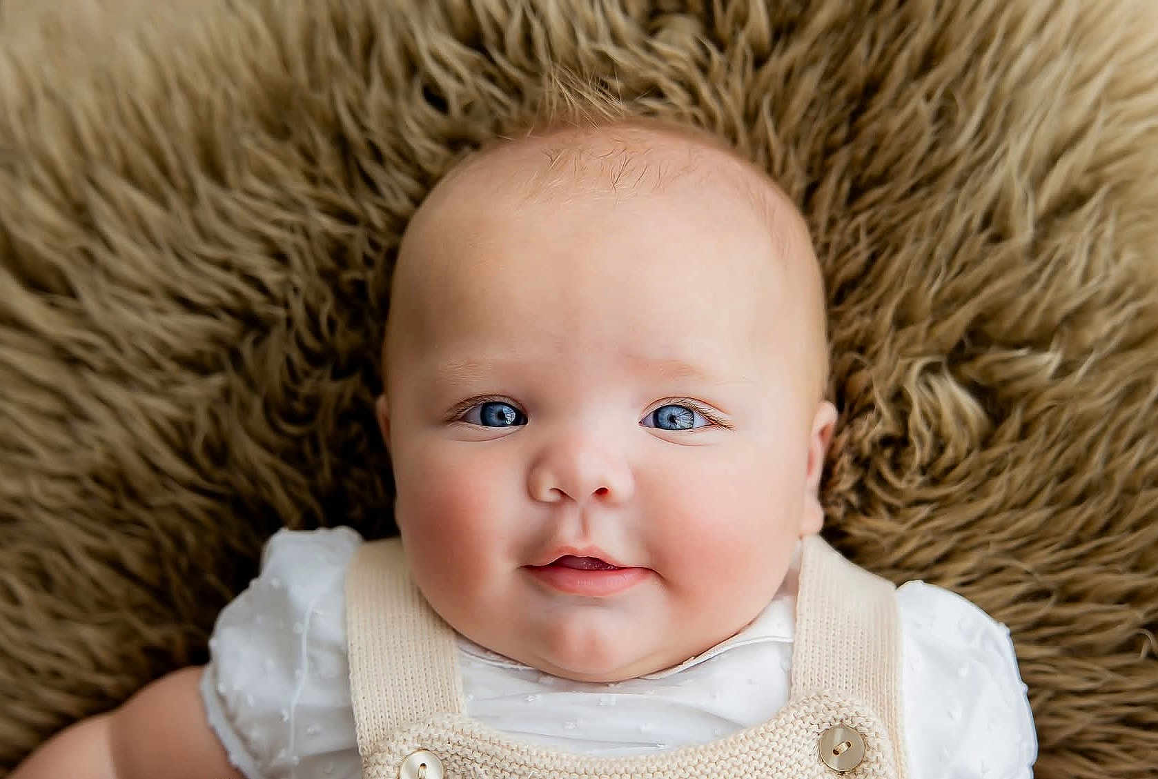 Michael is registered to the contest to win money with this photo: baby, infant, portrait, face, blue_eyes, smiling, cute, soft_texture, fur_background, clothing, knitwear, white_shirt, close_up, rosy_cheeks, skin, person, child, newborn, happy, innocence