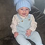 Aaron-Jay is registered to the contest to win money with this photo: baby, child, smiling, knitted_clothing, hat, pom_poms, overalls, sitting, couch, indoor, cute, happy, person, face, red_eye, warm_clothing, cozy, infant, portrait, furniture