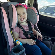 Sage is registered to the contest to win money with this photo: toddler, child, car_seat, pink_bow, seatbelt, car_interior, smile, happy, window, sunlight, toy, clothing, blue_pants, short_sleeve_shirt, headrest, car_door, seat, safety, portrait, daylight