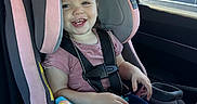 Sage is registered to the contest to win money with this photo: blue_pants, car_door, car_interior, car_seat, child, clothing, daylight, happy, headrest, pink_bow, portrait, safety, seat, seatbelt, short_sleeve_shirt, smile, sunlight, toddler, toy, window