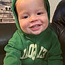 child, toddler, hoodie, green_clothing, smiling, face, indoor, living_room, sofa, clock, wall, framed_pictures, happy, cute, person, sweatshirt, young_child, candid, portrait, cozy