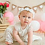 baby, balloon, celebration, child, crawling, cute, decorations, flower, headband, heart_bunting, indoor, lace, pink, portrait, roses, soft_lighting, white, white_dress, wood_floor, young_child