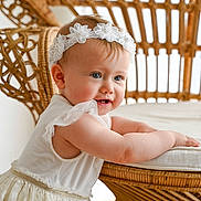 Aëlys participe au concours pour gagner de l'argent avec cette photo : arm, baby, background, child, curious, cute, face, flower, furniture, hands, happy, headband, indoor, natural_light, portrait, skin, smiling, toddler, white_dress, wicker_chair