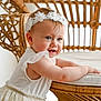 arm, baby, background, child, curious, cute, face, flower, furniture, hands, happy, headband, indoor, natural_light, portrait, skin, smiling, toddler, white_dress, wicker_chair