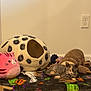 kitten, calico_cat, plush_toy, cat_cave, pink_pillow, brown_plush, blanket, halloween_theme, floor, wall, electrical_outlet, indoor, resting, feline, cute, cozy, pet, animal, sleeping, soft_toys