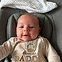 baby, infant, face, smile, onesie, clothing, seat, blanket, cute, expression, child, indoor, portrait, person, text, zebra_patch, happy, cozy, young, closeup