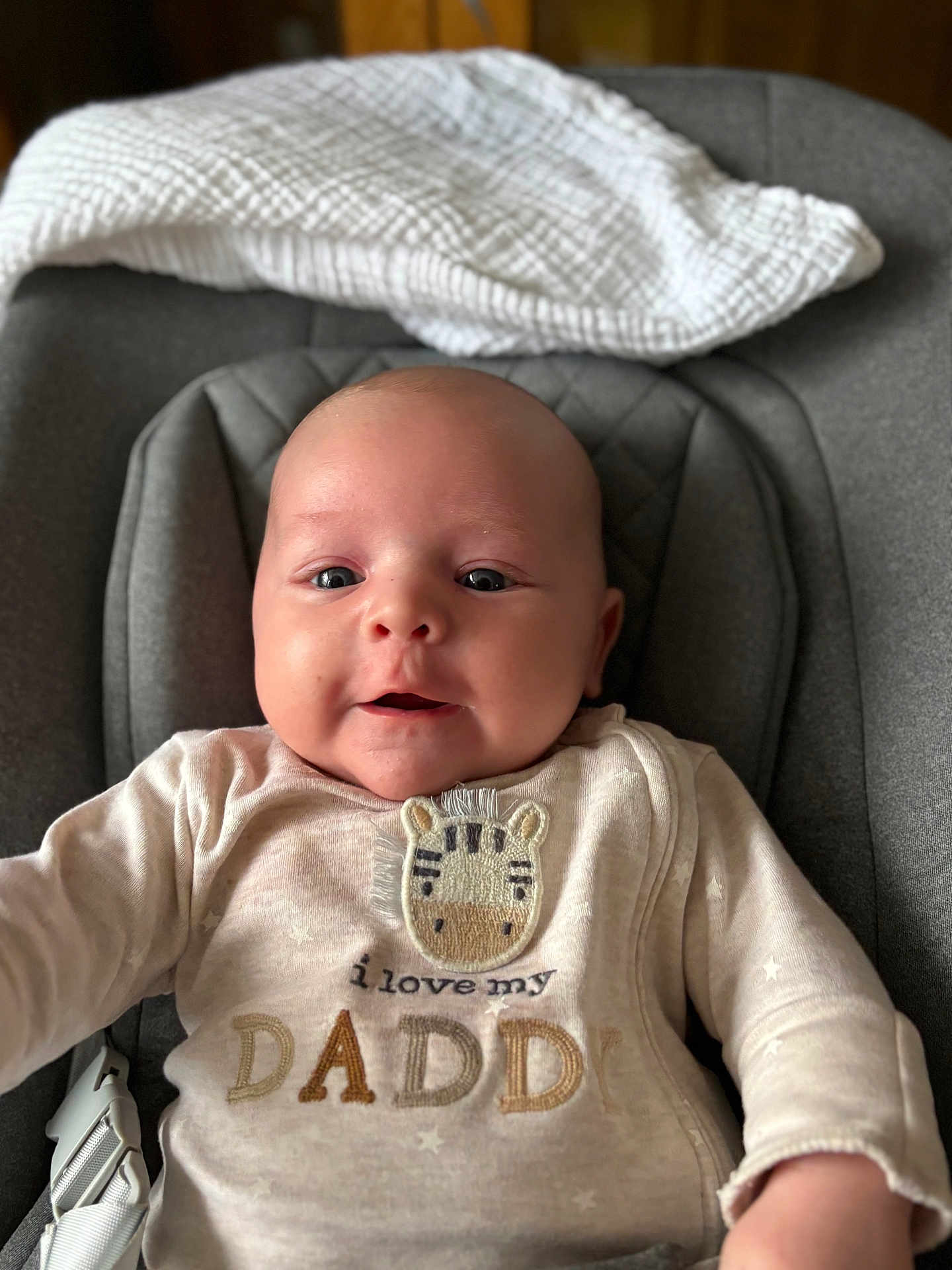 Morgan joined the competition — help win amazing prizes! baby, infant, face, smile, onesie, clothing, seat, blanket, cute, expression, child, indoor, portrait, person, text, zebra_patch, happy, cozy, young, closeup