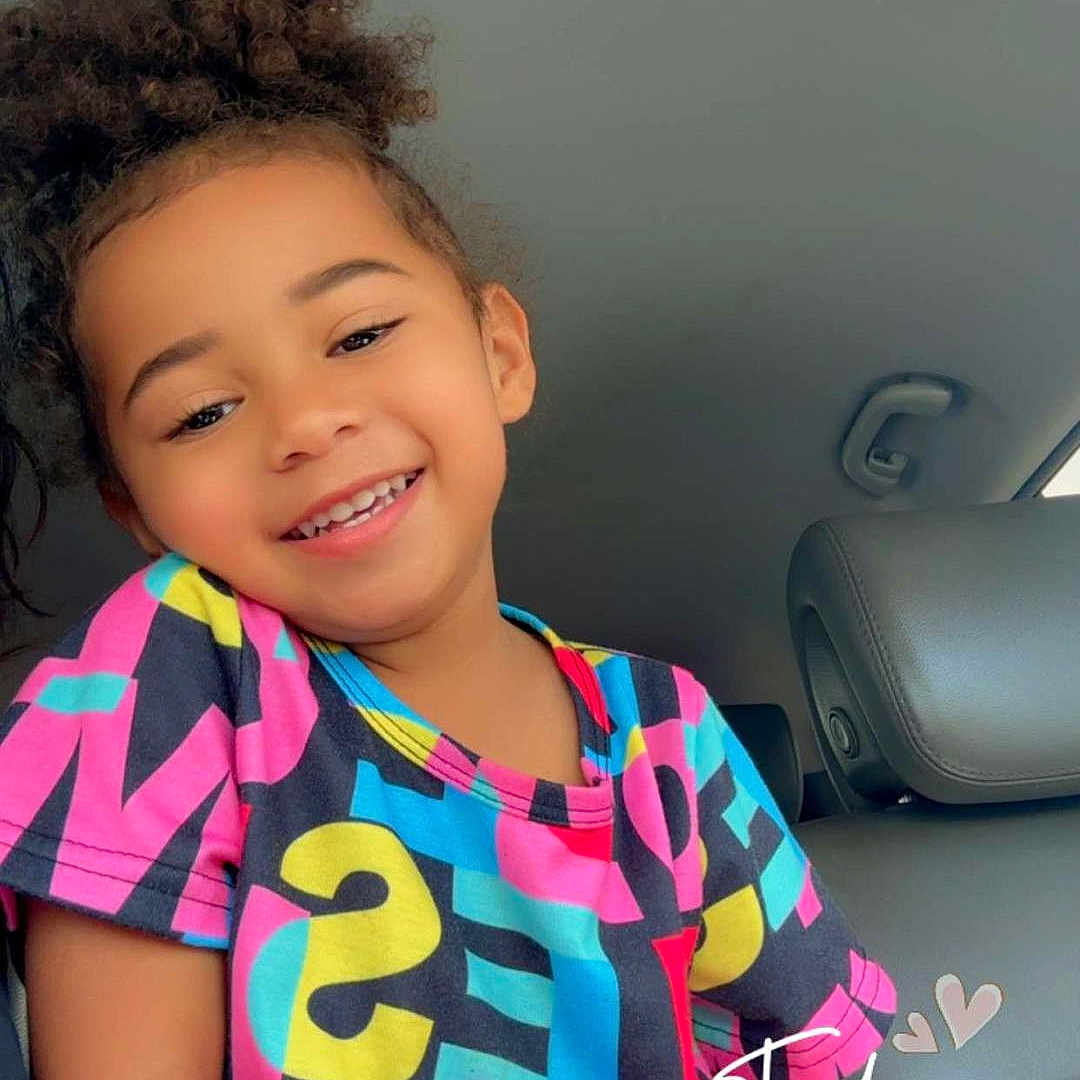 Olivianna is registered to the contest to win money with this photo: bodypart, child, clothing, cushion, dress, face, female, girl, hair, happy, head, homedecor, mouth, person, photography, portrait, sleeve, smile, t_shirt, teeth