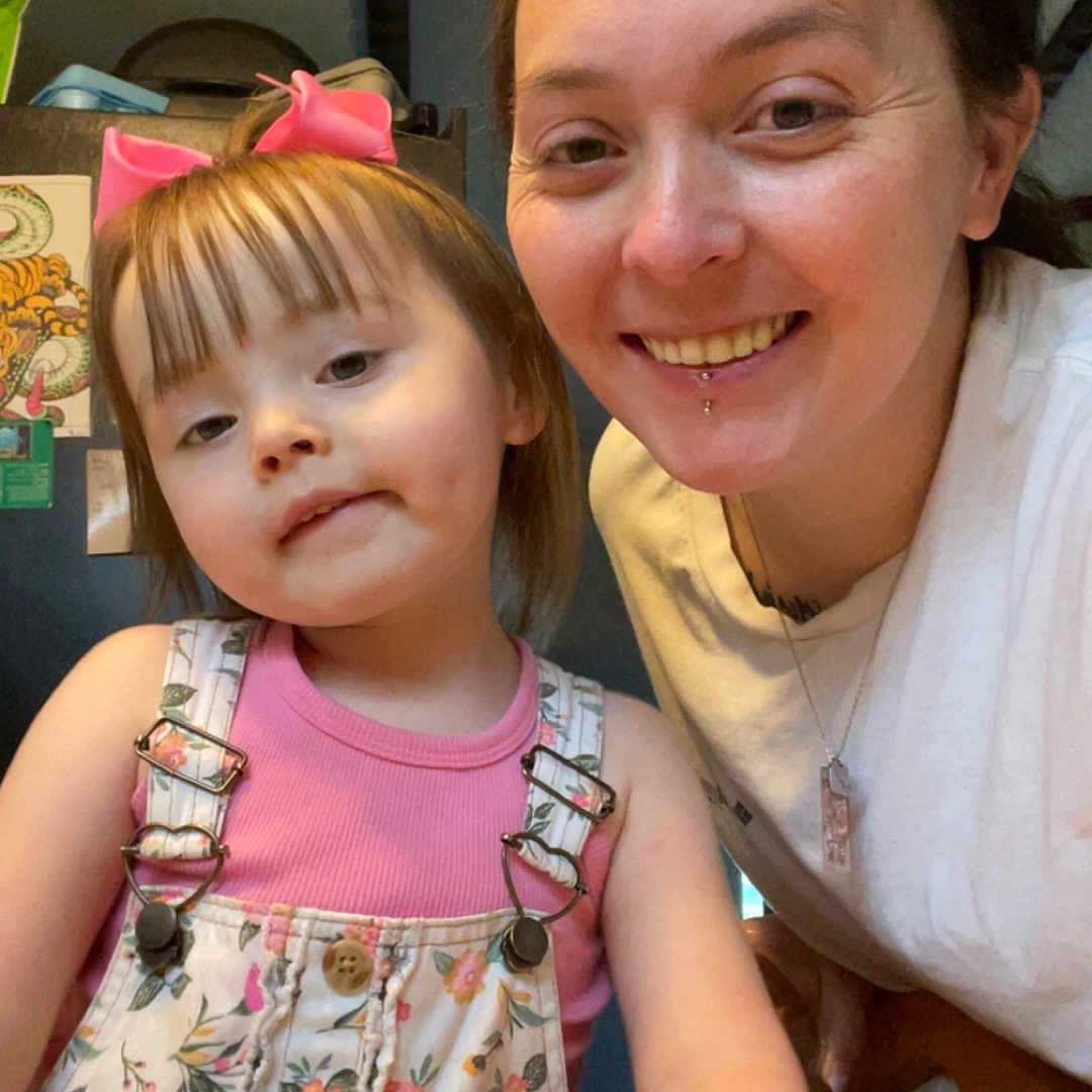 Aspen is registered to the contest to win money with this photo: adult, casual_clothing, chair, child, face, family, floral_overalls, hair, happy, indoor, lip_piercing, people, person, pink_bow, portrait, skin, smiling, table, woman, young_child