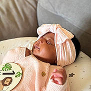 Janelle is registered to the contest to win money with this photo: baby, sleeping, headband, bow, pink, knitted_sweater, cushion, milestone_card, lion, stars, infant, peaceful, closeup, portrait, cute, one_month, child, soft_lighting, indoors, cozy