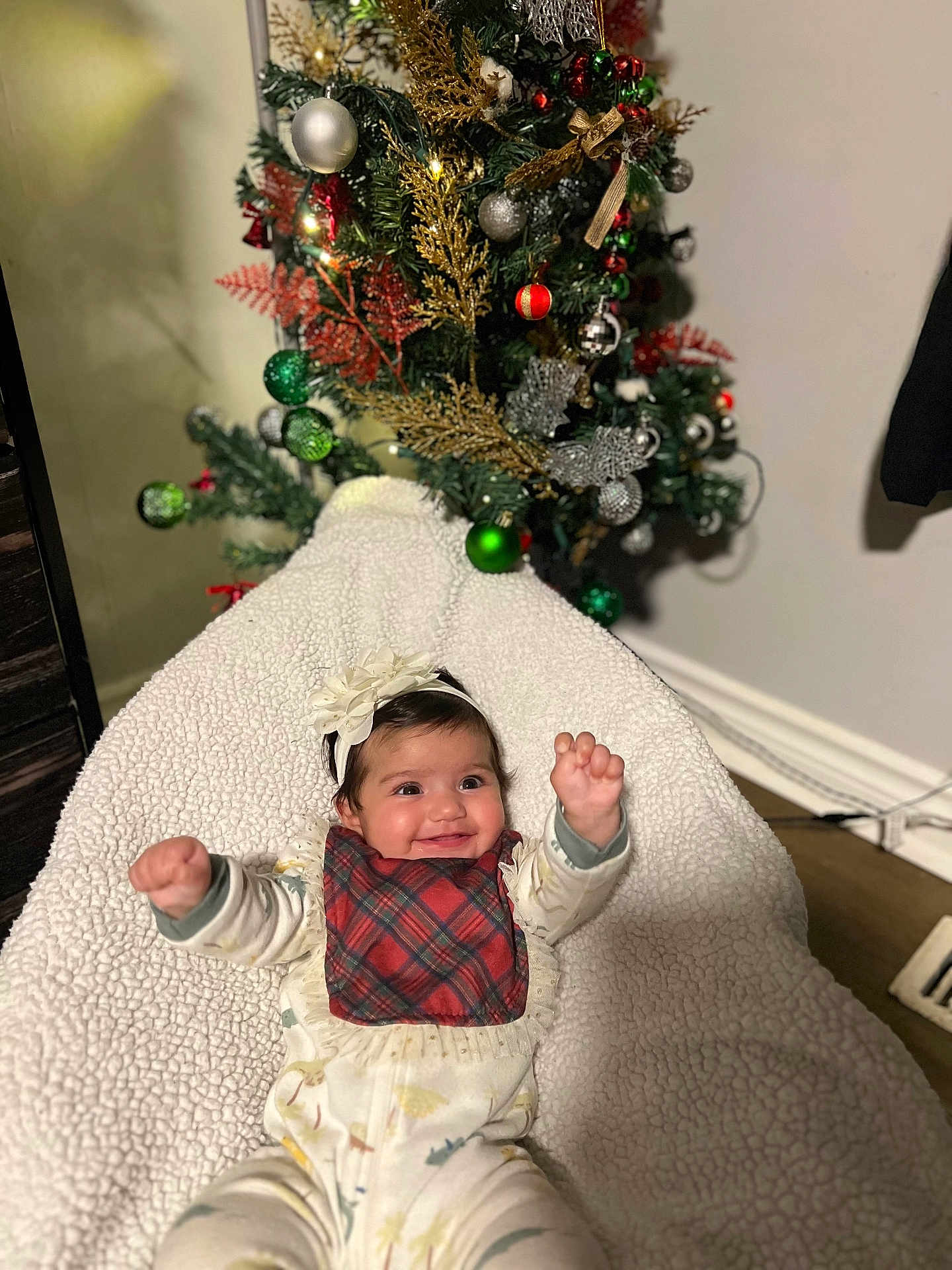 Zanara joined the competition — help win amazing prizes! baby, infant, smiling, happy, headband, plaid_bib, blanket, christmas_tree, ornaments, holiday, decorations, indoor, cozy, celebration, festive, child, person, cute, joyful, portrait