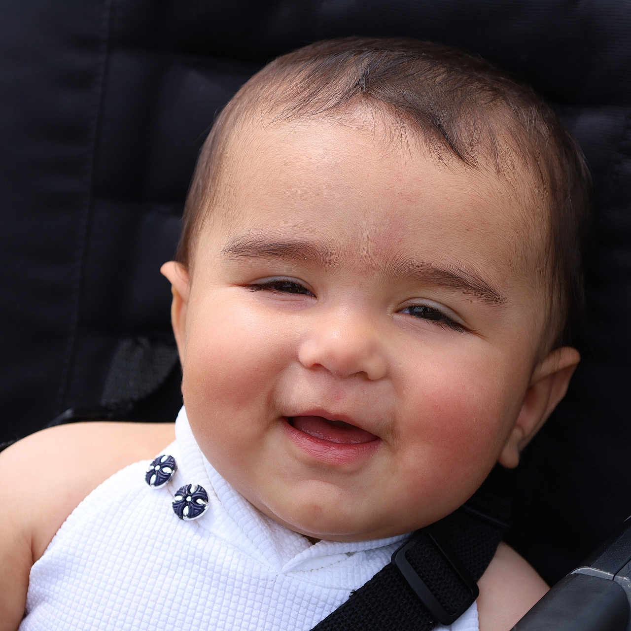 Vedika is registered to the contest to win money with this photo: baby, babywearing, button, cheek, child, closeup, clothing, cute, face, happy, head, infant, outdoor, person, portrait, seat, seatbelt, skin, smile, stroller