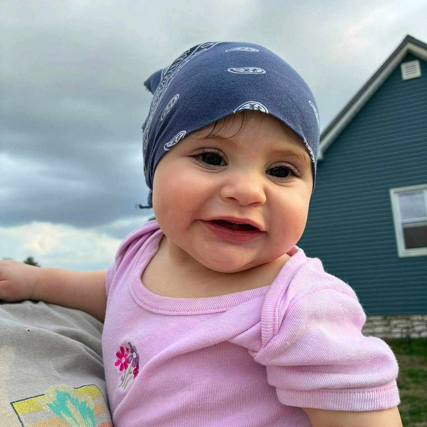 Ceylin is registered to the contest to win money with this photo: baby, child, bandana, pink_shirt, smile, drool, outdoor, house, blue_sky, cloudy, person, portrait, cute, holding, grass, headwear, face, cheerful, casual_clothing, daylight