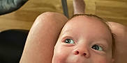 Tristan is registered to the contest to win money with this photo: baby, child, smile, face, person, yellow_shirt, legs, lap, wooden_floor, baby_seat, indoor, happy, cute, infant, looking_up, skin, head, eyes, mouth, expression