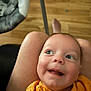 baby, child, smile, face, person, yellow_shirt, legs, lap, wooden_floor, baby_seat, indoor, happy, cute, infant, looking_up, skin, head, eyes, mouth, expression
