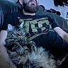 arm, beard, cat, couch, cozy, fur, glasses, hat, indoor, living_room, looking_up, person, pet, portrait, relaxing, sitting, sofa, t_shirt, tabby_cat, whiskers