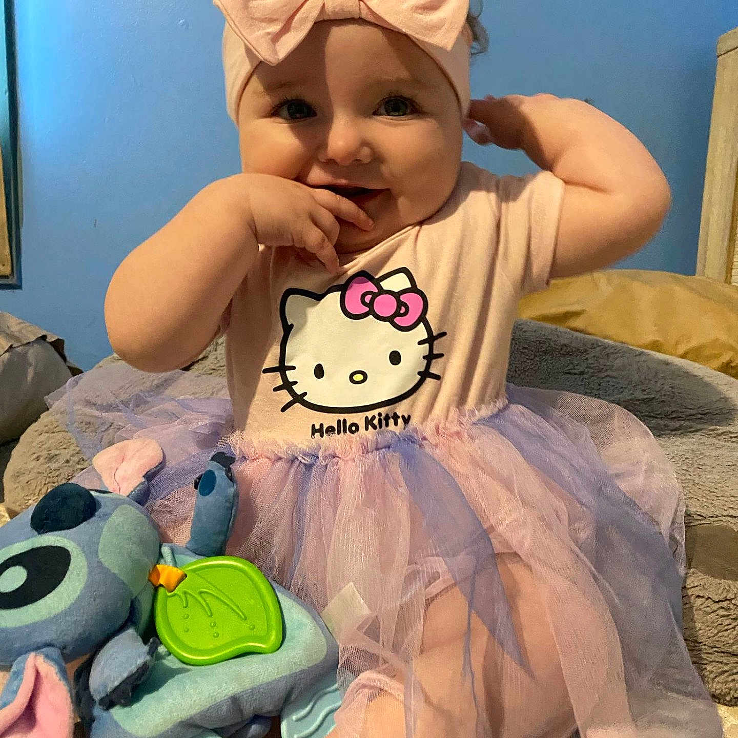Aylah-Joan joined the competition — help win amazing prizes! baby, blue_wall, child, cozy, cute, dress, hand_on_face, headband, hello_kitty, indoor, infant, pink, playful, plush_toy, purple, sitting, smiling, soft_toys, stitch, tutu