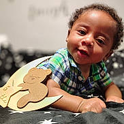Octavious is registered to the contest to win money with this photo: baby, infant, child, plaid_shirt, smiling, lying_down, blanket, star_pattern, wooden_decoration, bear, 5_months, cute, indoors, portrait, face, hand, curly_hair, cozy, soft_lighting, closeup