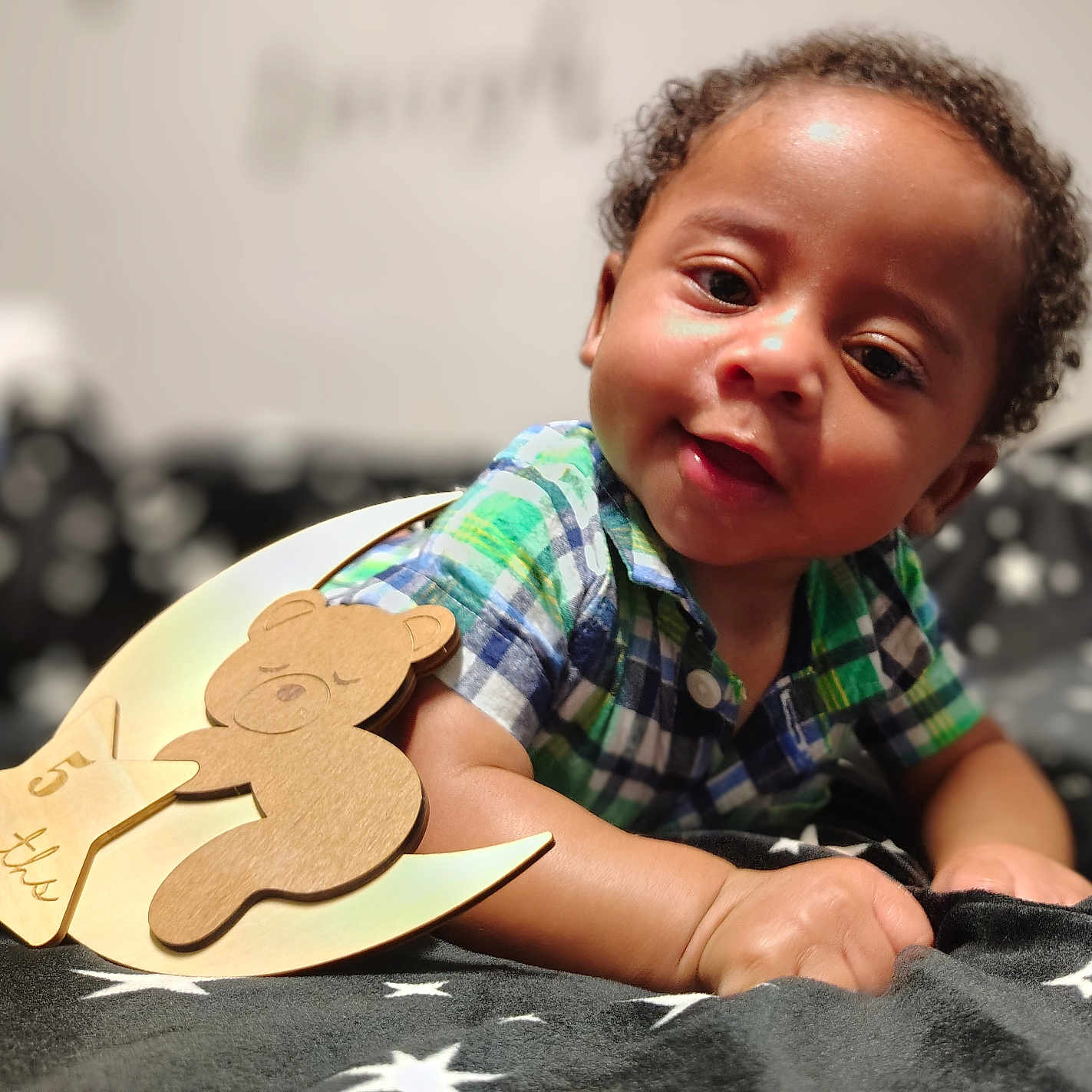Octavious is registered to the contest to win money with this photo: 5_months, baby, bear, blanket, child, closeup, cozy, curly_hair, cute, face, hand, indoors, infant, lying_down, plaid_shirt, portrait, smiling, soft_lighting, star_pattern, wooden_decoration