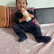 Zouleikha participe au concours pour gagner de l'argent avec cette photo : toddler, baby, milk_bottle, smiling, onesie, blanket, pillow, striped_pillow, couch, indoor, child, happy, sitting, face, person, cozy, home, cute, portrait, infant