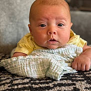 Jax joined the competition — help win amazing prizes! baby, infant, blanket, cloth, hand, face, eyes, indoor, carpet, person, skin, yellow_clothing, texture, soft, cute, lying_down, closeup, portrait, expression, child