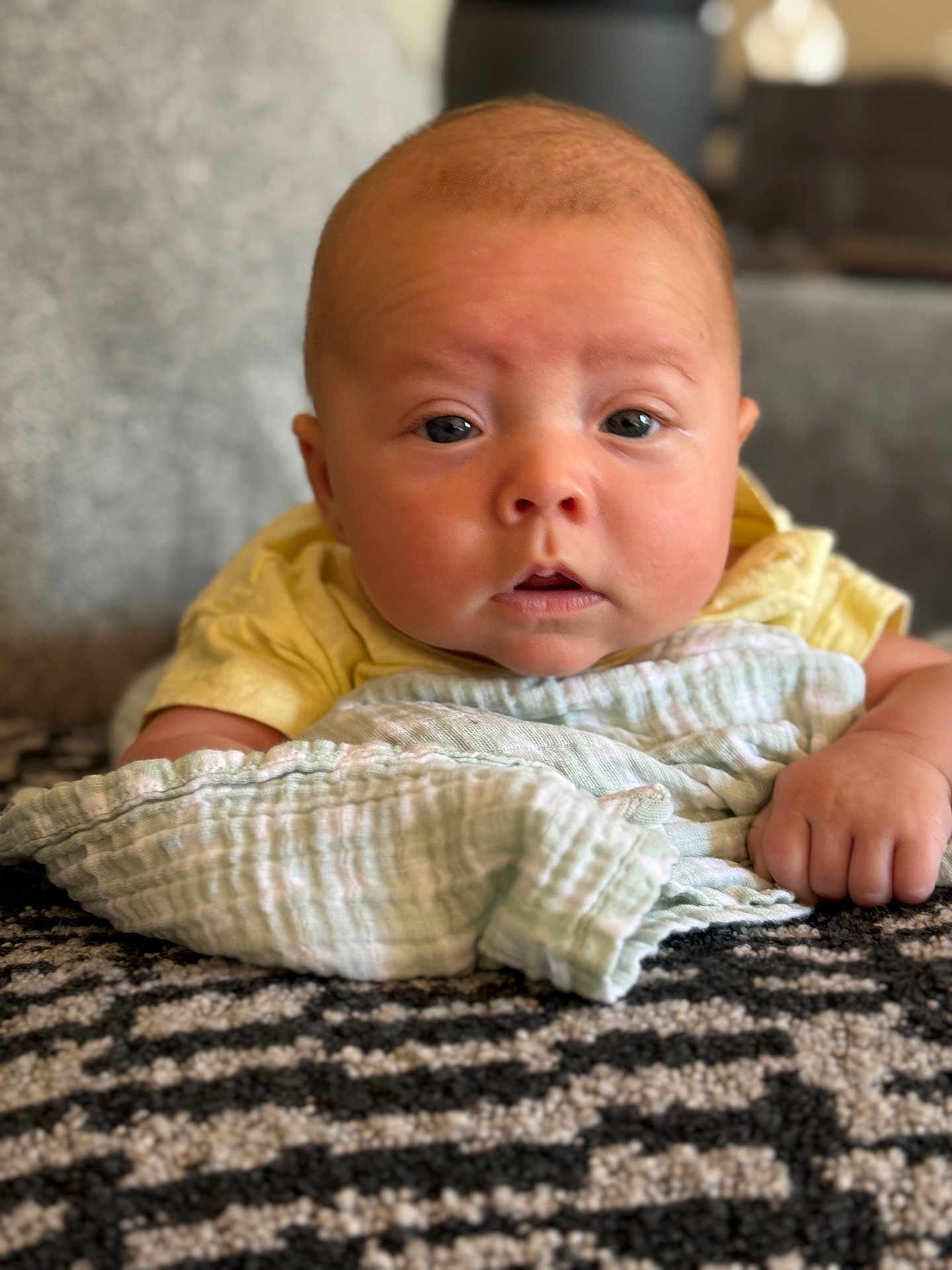 Jax joined the competition — help win amazing prizes! baby, infant, blanket, cloth, hand, face, eyes, indoor, carpet, person, skin, yellow_clothing, texture, soft, cute, lying_down, closeup, portrait, expression, child