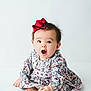 baby, infant, toddler, bow, hair_bow, floral_dress, patterned_clothing, sitting, barefoot, toes, open_mouth, surprised_expression, portrait, studio, white_background, cute, adorable, long_sleeves, one_person, hands