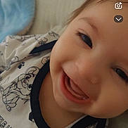 Ghaith is registered to the contest to win money with this photo: baby, infant, smile, close_up, face, teeth, onesie, patterned_clothing, paw_print, bed, pillow, blanket, happy, cute, portrait, indoor, lying_down, expression, soft_lighting, candid