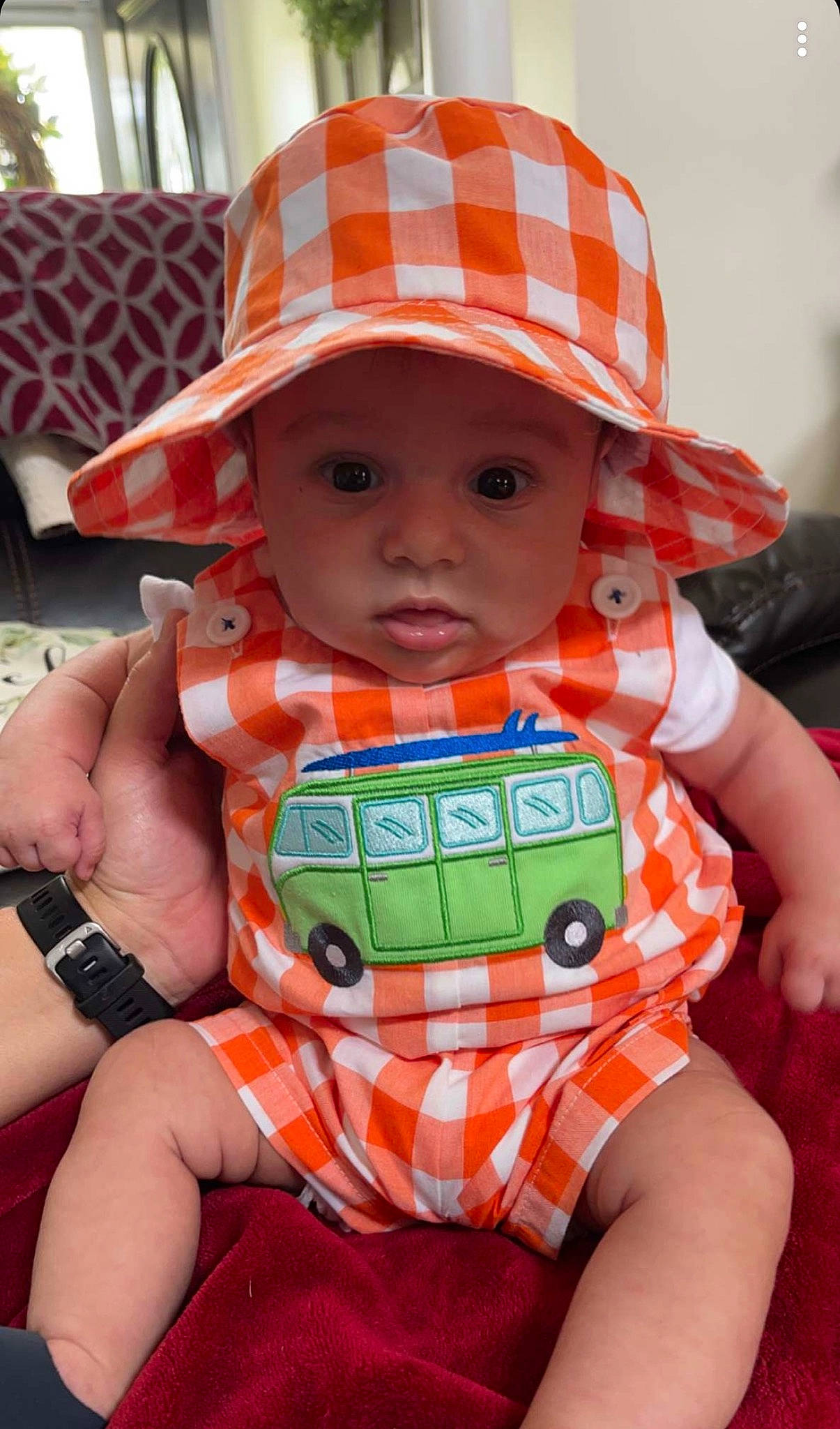 Adam is registered to the contest to win money with this photo: baby, baby_carriage, baby_toddler_clothing, cap, child, fashion_accessory, finger, hat, headgear, headwear, helmet, orange, person, personal_protective_equipment, pink, plaid, red, sitting, skin, sun_hat