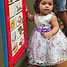 Ciara is registered to the contest to win money with this photo: toddler, child, girl, dress, purple_bow, playground, play_panel, carpet, curious, indoor, person, footwear, sock, shorts, adult, pattern, floral, colorful, toy, exploring
