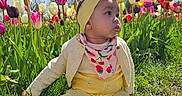 Odie is registered to the contest to win money with this photo: baby, child, tulip, flower, grass, outdoor, nature, blue_sky, clouds, yellow_clothing, headband, barefoot, greenery, spring, sunlight, portrait, sitting, colorful, garden, cute
