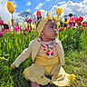 baby, child, tulip, flower, grass, outdoor, nature, blue_sky, clouds, yellow_clothing, headband, barefoot, greenery, spring, sunlight, portrait, sitting, colorful, garden, cute