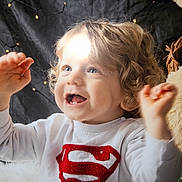 Gabin a rejoint le concours — aidez-le/la à gagner de superbes lots ! toddler, child, curly_hair, superman_logo, white_shirt, smiling, bubbles, fairy_lights, teddy_bear, indoor, happy, cute, portrait, baby, hands_up, playful, cozy, background, soft_lighting, expression