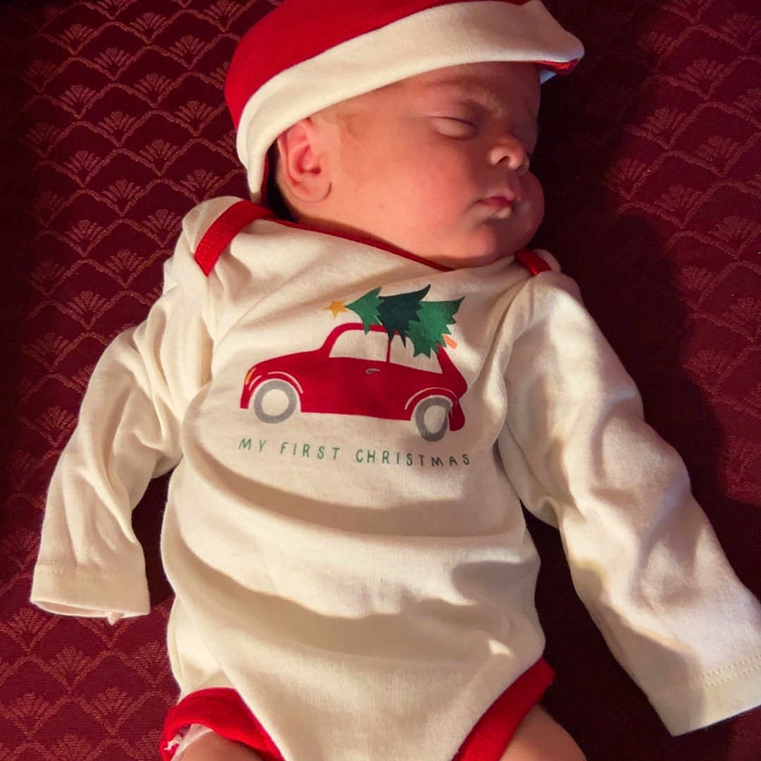 Enzo is registered to the contest to win money with this photo: baby, child, christmas, clothing, cozy, cute, fabric, festive, holiday, indoors, infant, lying_down, maroon, onesie, peaceful, portrait, red, santa_hat, sleeping, white