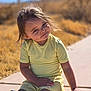 child, toddler, sitting, yellow_clothing, outdoor, sidewalk, sunlight, smile, face, hair, grass, nature, casual, happy, young, person, daylight, cute, playful, portrait