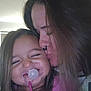 child, woman, kiss, pacifier, smile, indoor, love, affection, hair, face, closeup, happy, family, bond, person, pink_clothing, nose_ring, long_hair, toddler, emotion