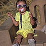toddler, child, yellow_clothing, sunglasses, pacifier, outdoor, bench, plush_toy, shoes, relaxed_pose, sunlight, reflection, grass_background, shorts, casual, baby_accessory, seat, summer, cute, playful